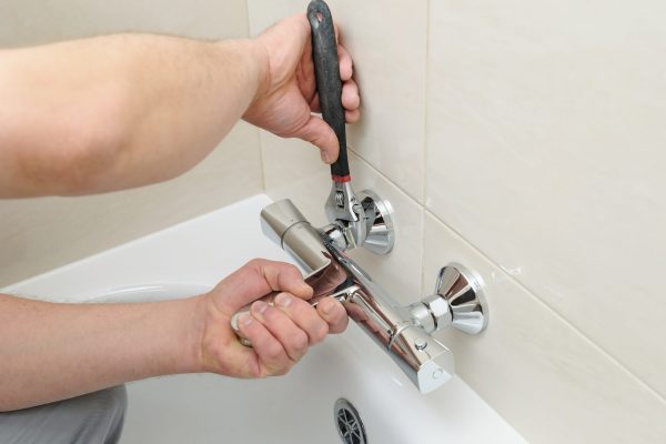 Installing faucet with thermostat. Man's hands are fixing bath tap into place.
